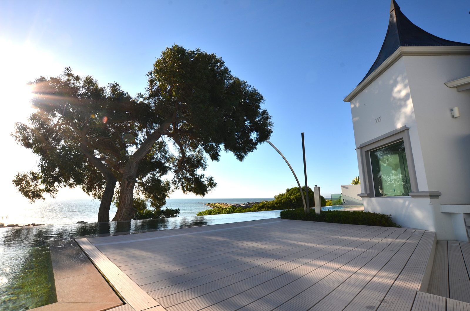 Holzterrasse am Infinity-Pool mit grossem Baum, Meer und Türmchen des Hauses